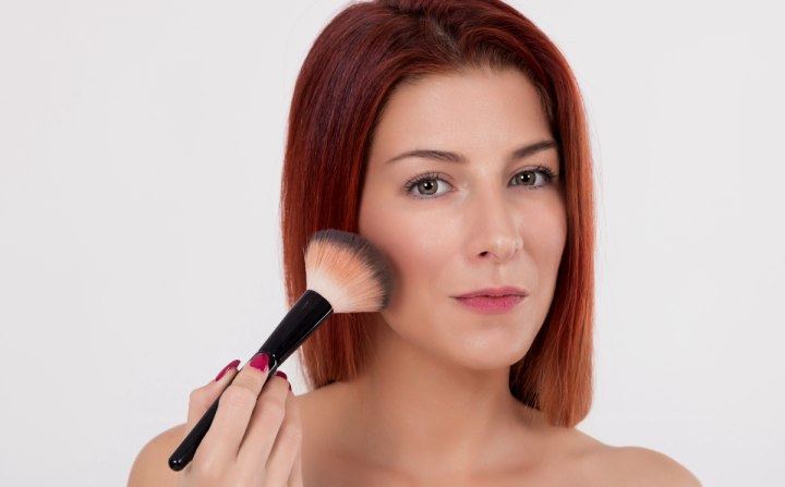 Woman who is applying make-up to enhance her cheekbones