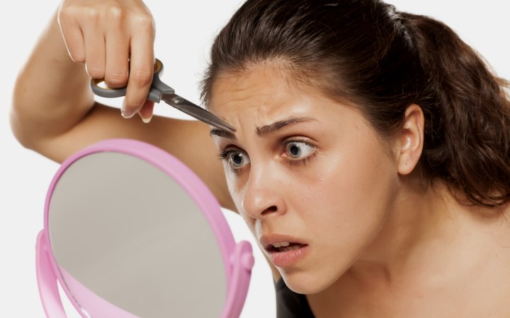 Girl who is trimming her eyebrows with scissors